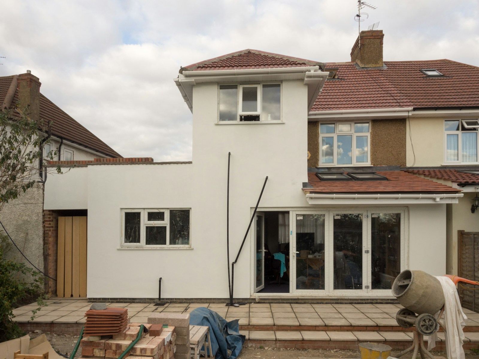 Woning met een wit bepleisterde uitbouw tijdens renovatiewerken, met een betonmolen ervoor